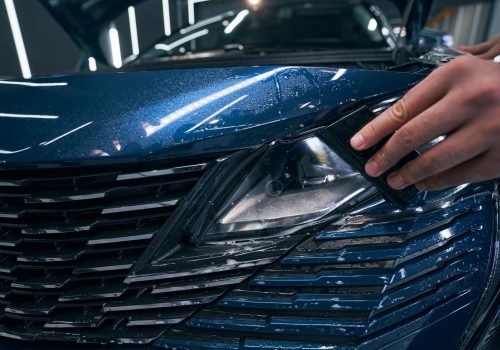 Closeup car service worker installing PPF with squeegee on headlight